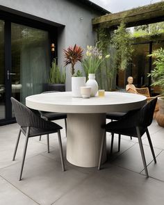 a white table with chairs around it in front of a building and some potted plants