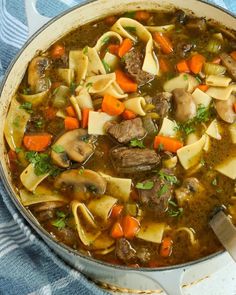 a pot filled with pasta and meat soup on top of a blue towel next to a wooden spoon