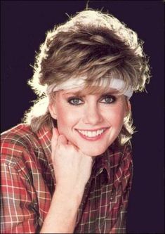 an older woman with short hair wearing a plaid shirt and smiling at the camera while leaning on her elbow