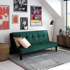 a green futon sofa sitting in a living room next to a lamp and pictures on the wall