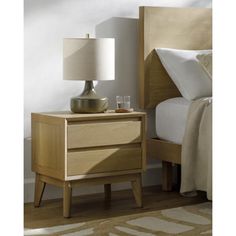 a night stand with a lamp on it next to a bed