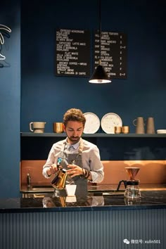 a man pouring coffee into a cup at a counter in front of a blue wall