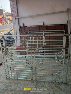 an old metal fence sitting on the side of a building next to a motorcycle parked in front of it