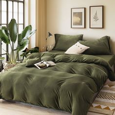 a bed with green comforter and pillows in a room next to a large window