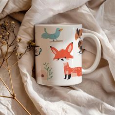 a coffee mug with foxes and birds on it next to some dried flowers in the foreground