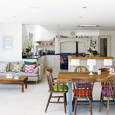 a living room filled with furniture next to a kitchen and dining room table covered in colorful pillows