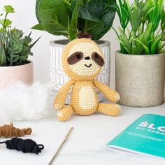 a crocheted slotty doll sitting next to a potted plant and knitting needles