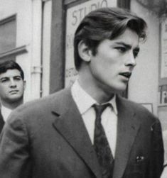 a man in a suit and tie walking down the street with another man behind him