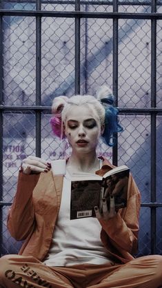 a woman sitting in front of a jail cell holding a book and looking at her phone