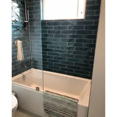 a bath tub sitting next to a toilet under a window in a bathroom with blue tiles on the walls