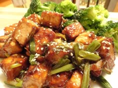 a white plate topped with tofu and broccoli covered in sesame seed flakes