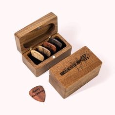 an open wooden box with four pieces of wood in it and a guitar picker next to it