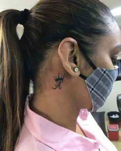 a woman with a tattoo on her neck and behind her ear, wearing a pink shirt