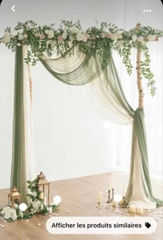 a wedding arch decorated with greenery and white flowers on the floor next to candles