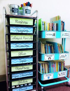 a stack of books with bins and labels on the bottom shelf in front of a wall