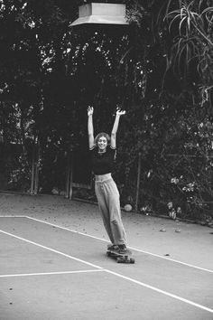 a woman riding a skateboard on top of a tennis court with her arms in the air