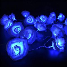 blue roses are glowing in the dark on a black surface with string lights around them