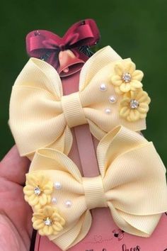 a hand holding a small yellow bow on top of a piece of pink paper with pearls