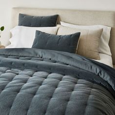 a bed with blue comforter and pillows on it in a white room next to a plant