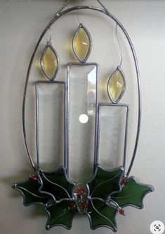 a lighted candle holder with holly leaves on the front and sides, hanging from a wall