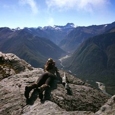 a woman sitting on top of a mountain next to a valley