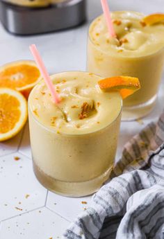 two glasses filled with orange smoothie next to sliced oranges