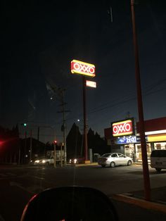 a gas station at night with cars parked in the lot and an oxo sign