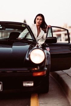 a woman leaning on the hood of a black sports car with her hand on the door handle