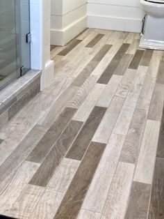 a white toilet sitting next to a shower in a bathroom on top of a hard wood floor