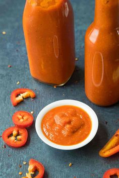 two jars of tomato sauce next to some sliced tomatoes and peppers on a blue surface