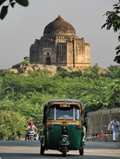 an old tuk - tuk driving down the road in front of a large building