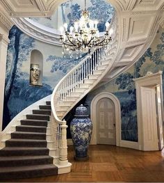 an ornate staircase with blue and white wallpaper in the foyer, next to a chandelier