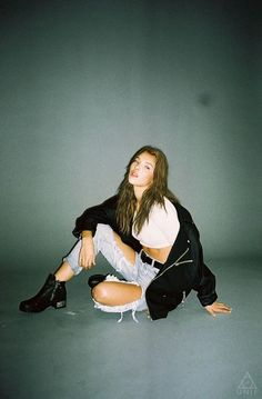 a young woman sitting on the ground with her legs crossed, wearing black boots and a white shirt