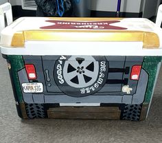 the back end of a cooler with wheels painted on it's sides, sitting on top of a carpeted floor