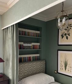 a bedroom with green walls and bookshelves above the bed, along with two framed pictures on the wall