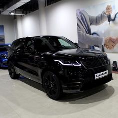 a black range rover is parked in front of a large poster with two men shaking hands