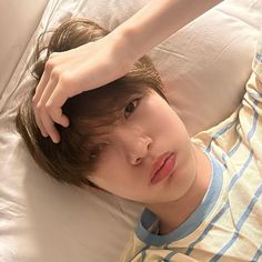 a young man laying on top of a bed next to a white pillow holding his hand over his head