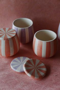 four ceramic cups and two plates on a pink surface, one with an umbrella design