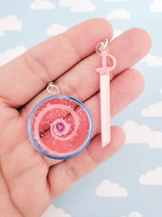 a hand holding a pink and blue keychain with an object in the middle