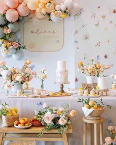 a table topped with lots of fruit and flowers next to a wall covered in balloons