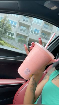 a woman sitting in a car holding a pink drink