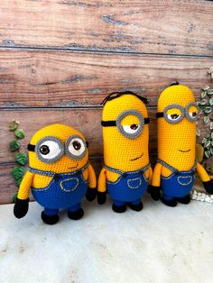 three crocheted minion dolls sitting next to each other in front of a wooden wall