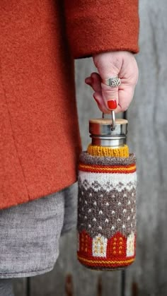 a woman is holding a bottle with a knitted sweater on it and a ring in her hand