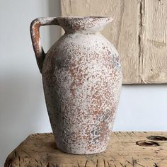 a white and brown vase sitting on top of a wooden table next to a painting