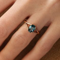 a woman's hand wearing a gold ring with a blue stone in the middle