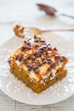 a white plate topped with a piece of cake covered in frosting and chocolate chips