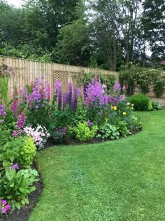 a garden filled with lots of flowers next to a lush green field and wooden fence