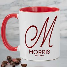 a red and white coffee mug sitting on top of a counter next to some coffee beans