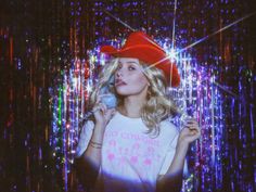 a woman wearing a red hat while talking on a cell phone in front of colorful lights