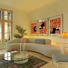 a living room filled with furniture next to a window covered in plants and paintings on the wall